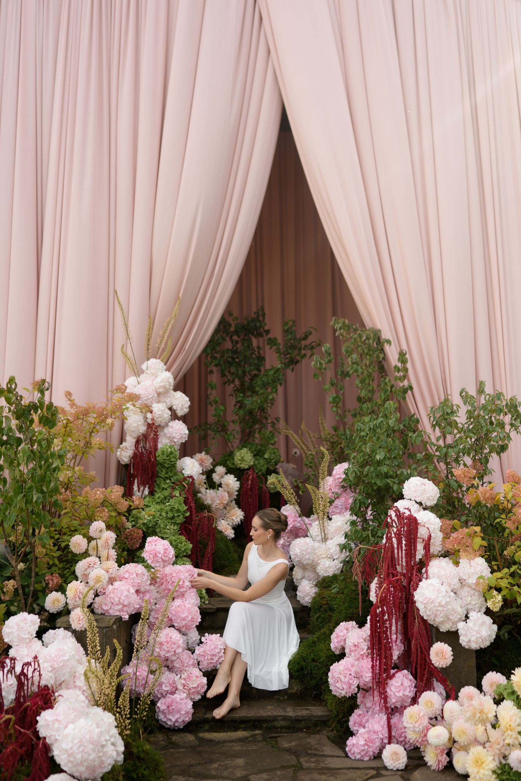 Soft pink garden wedding ceremony with a fully draped house facade, garden-style hydrangea florals, and elegant outdoor seating.