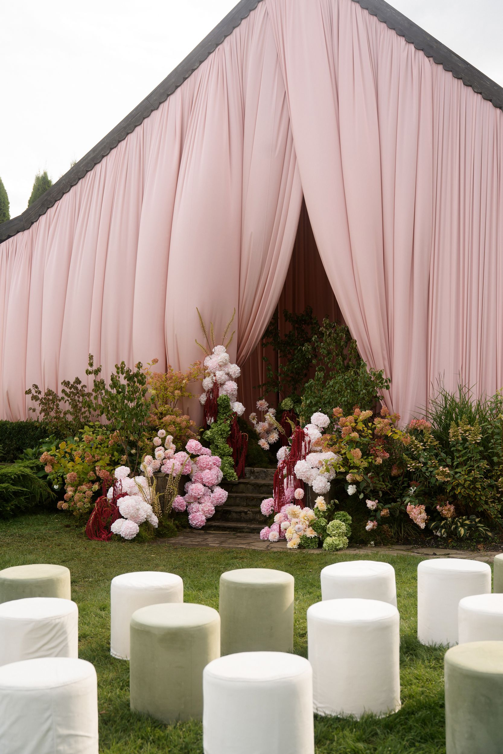 Soft pink garden wedding ceremony with a fully draped house facade, garden-style hydrangea florals, and elegant outdoor seating.