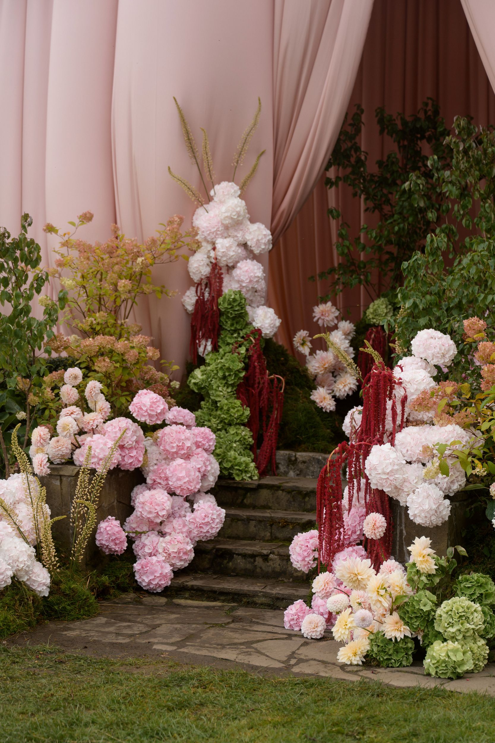 Soft pink garden wedding ceremony with a fully draped house facade, garden-style hydrangea florals, and elegant outdoor seating