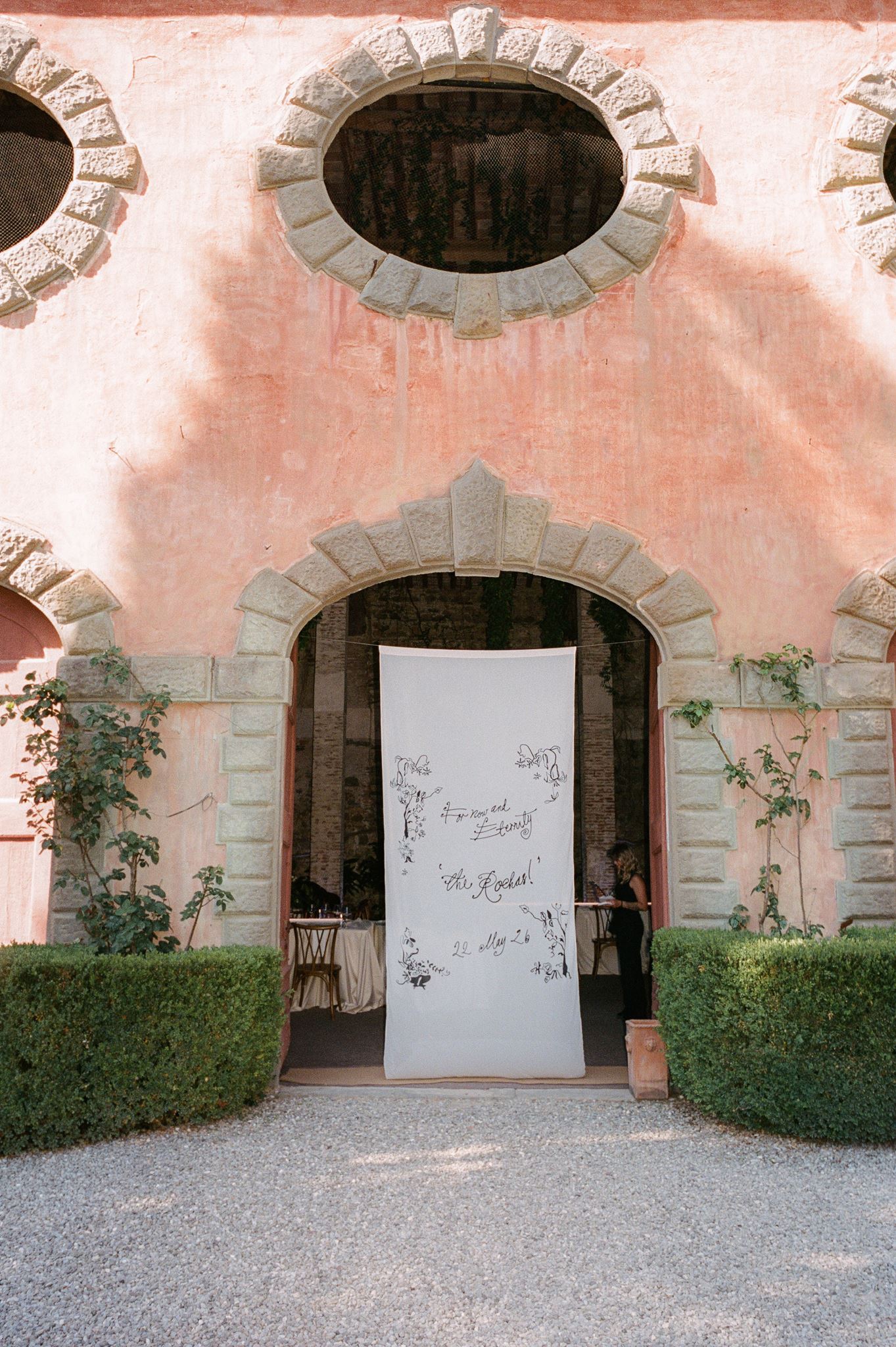 Hand-lettered wedding welcome sign hanging at the entrance of a pink Italian villa