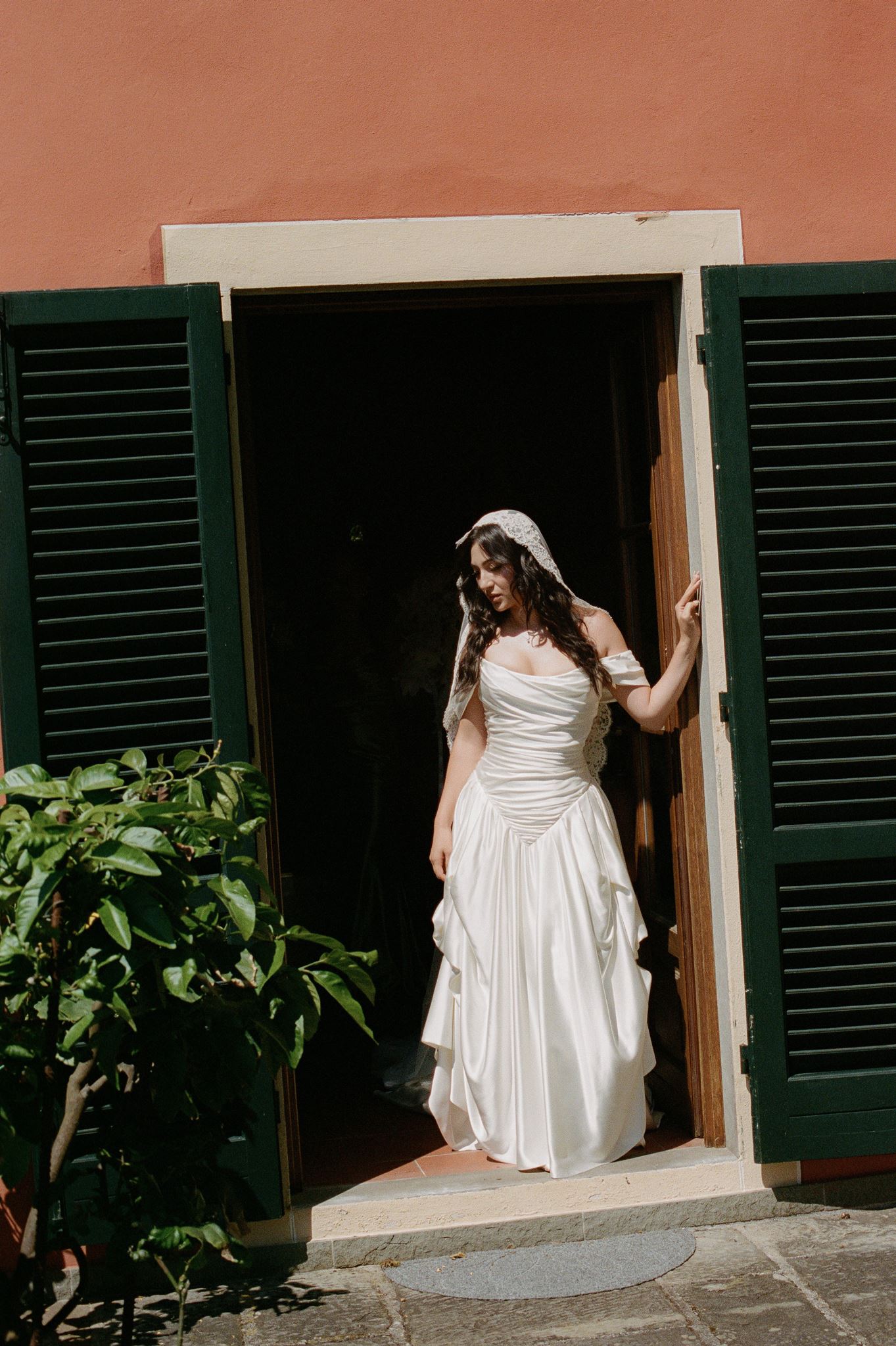 Bride in a ruched white wedding gown and lace veil standing in the doorway of an Italian villa