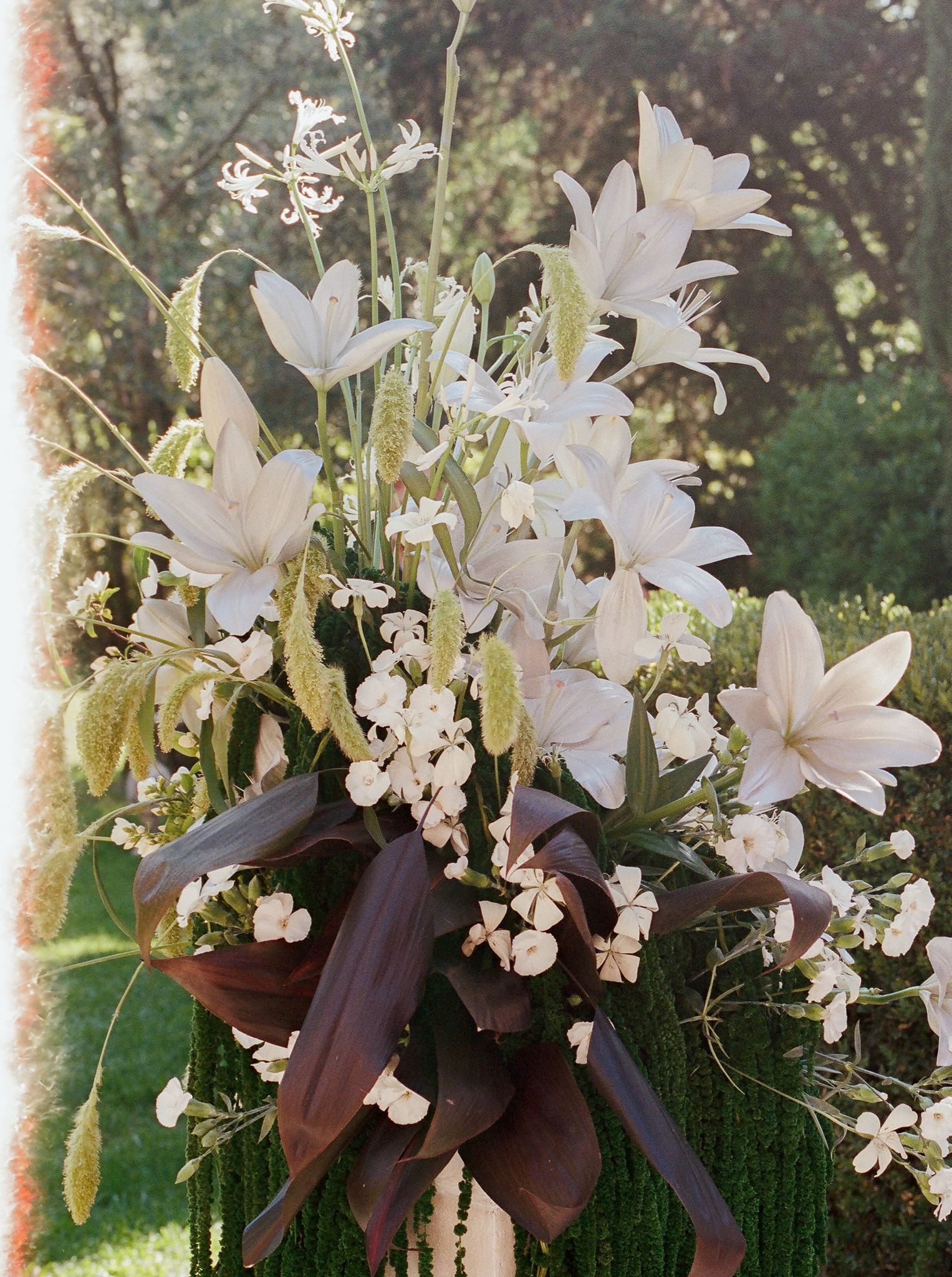 Sculptural white lily wedding arrangement with cascading green amaranthus and dark foliage