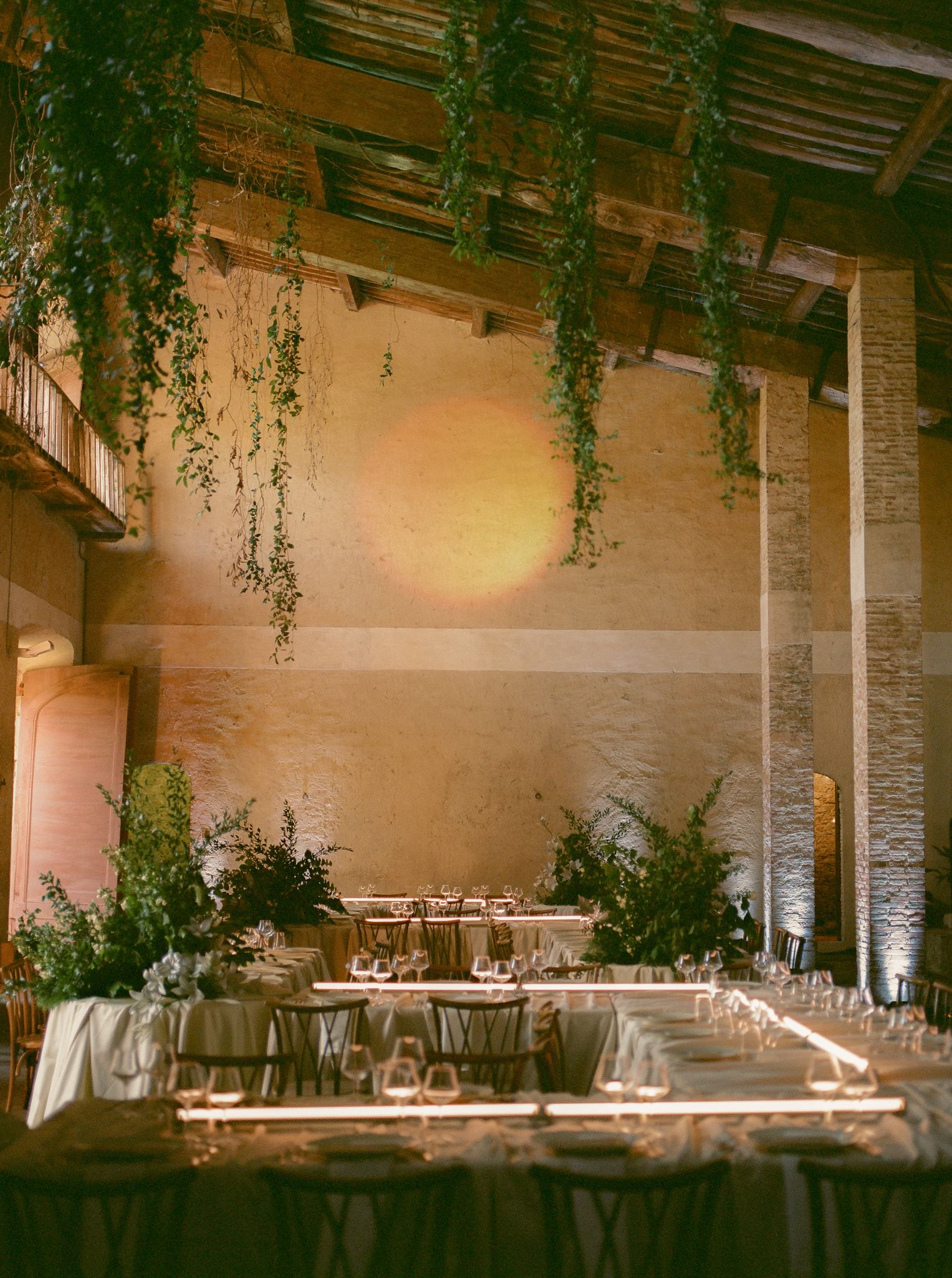 Modern wedding reception tables with white linens, sculptural greenery, linear lighting, and a moon projection backdrop