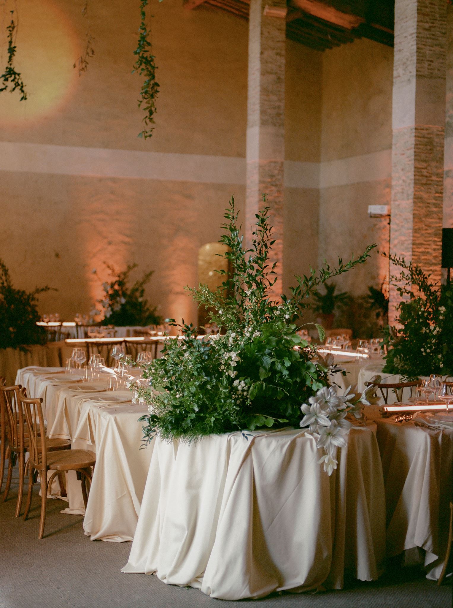 Modern wedding reception tables with white linens, sculptural greenery, linear lighting, and a moon projection backdrop