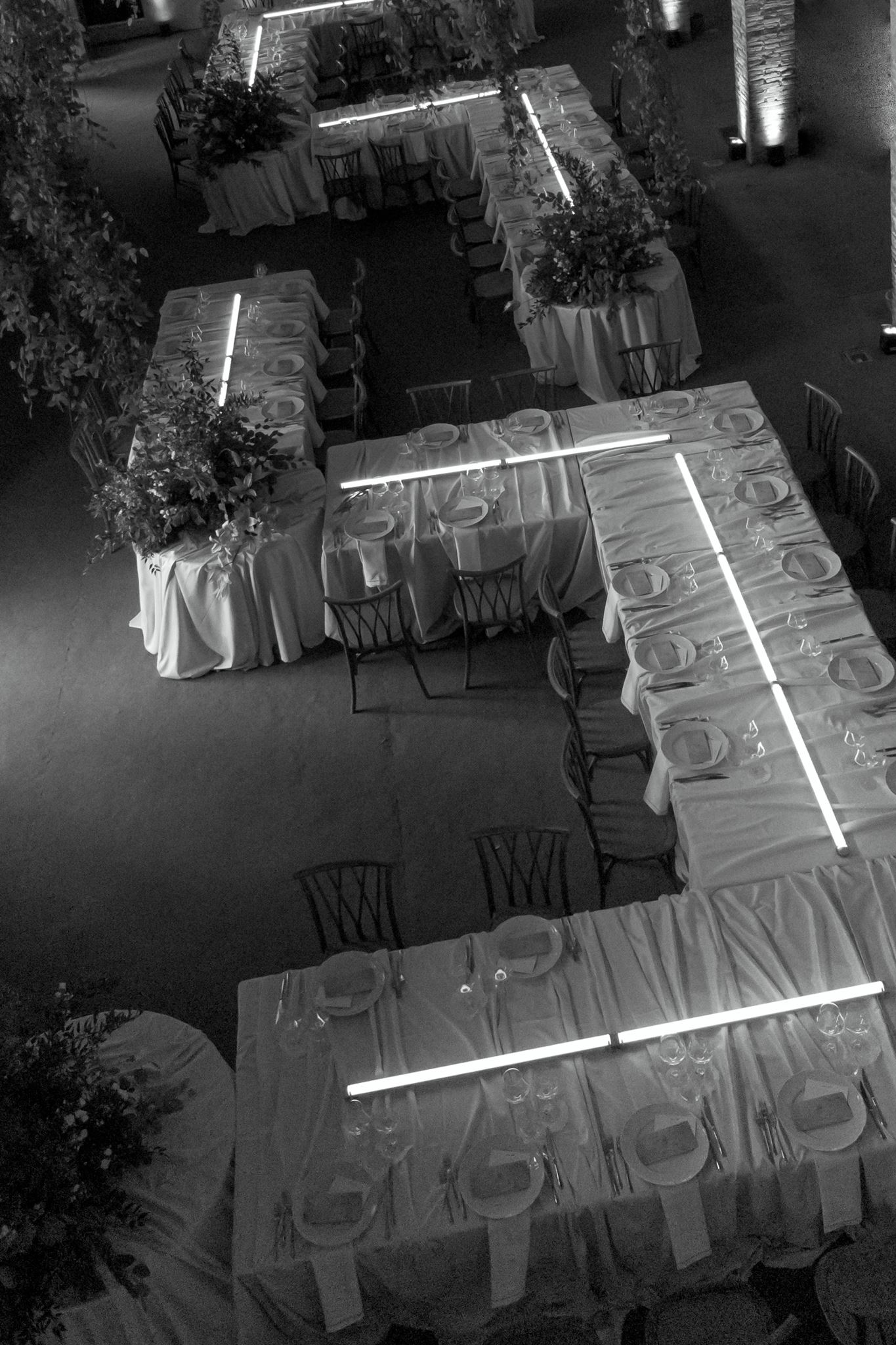Modern wedding reception tables with white linens, sculptural greenery, linear lighting, and a moon projection backdrop