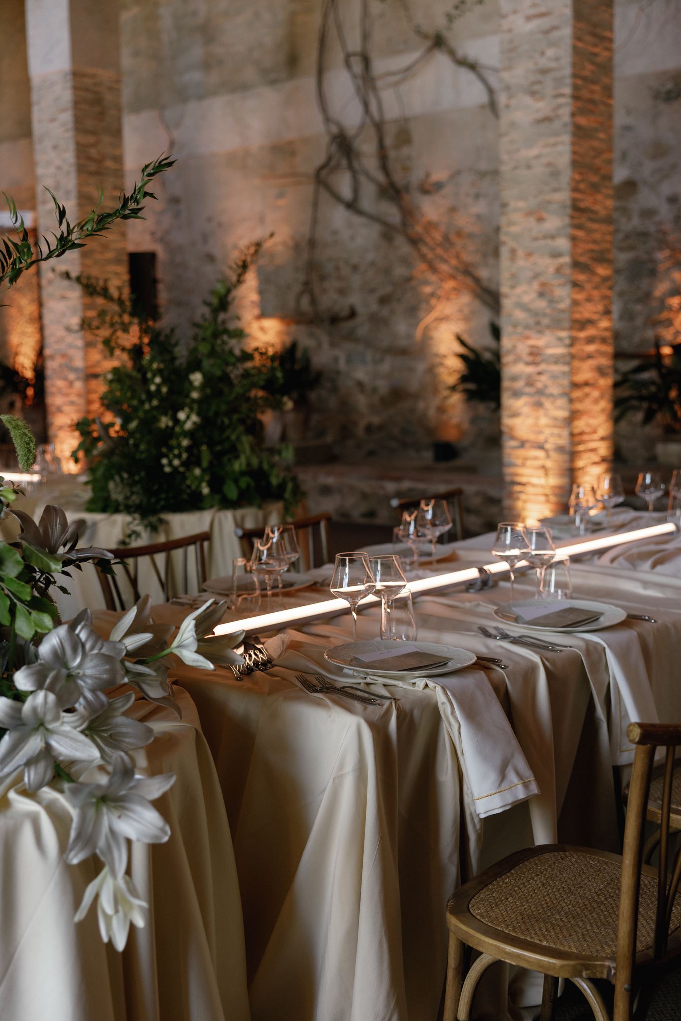 Modern wedding reception tables with white linens, sculptural greenery, linear lighting, and a moon projection backdrop
