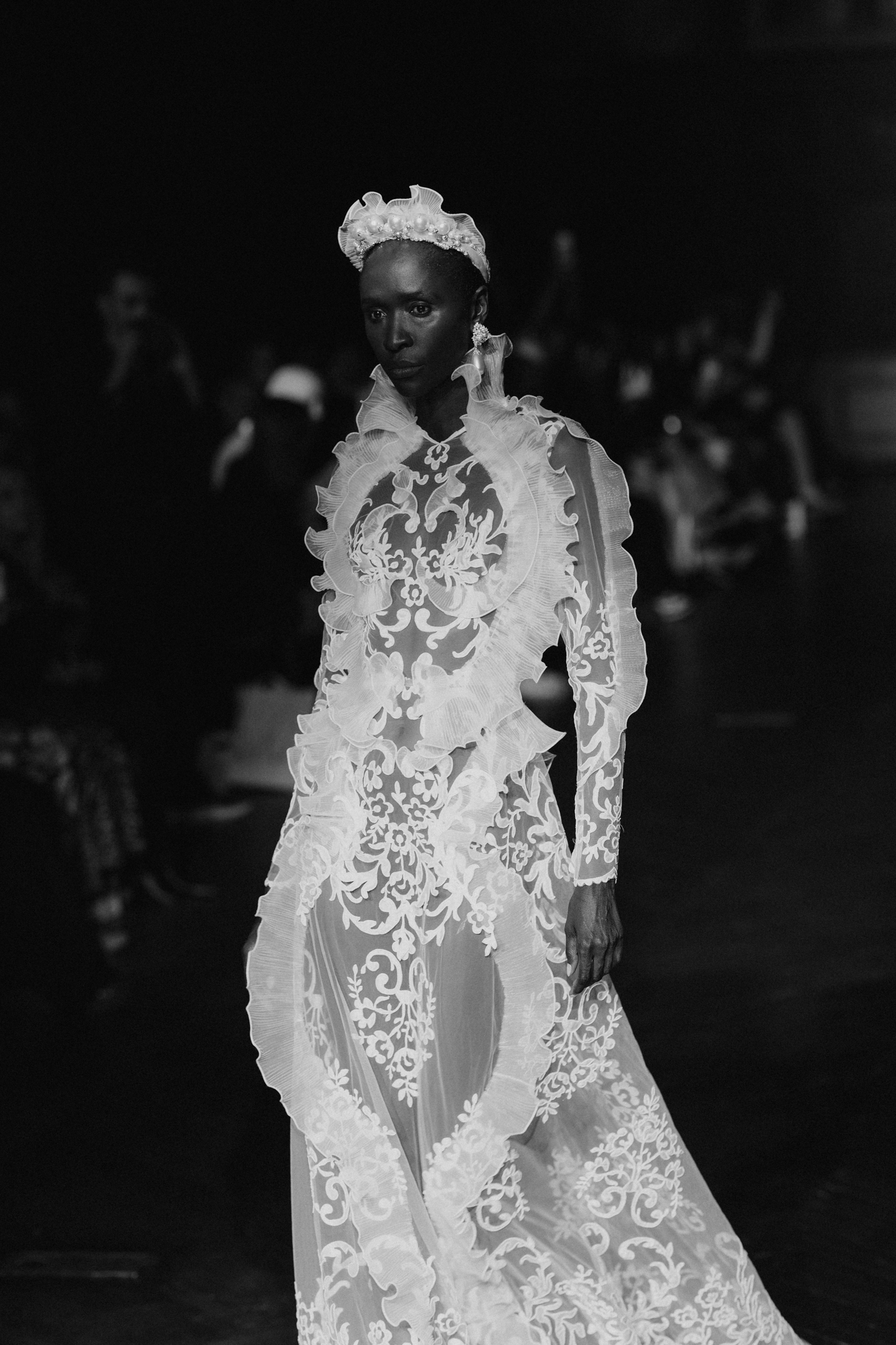 Black-and-white runway photograph of an ornate white bridal ensemble covered in dimensional floral embellishments
