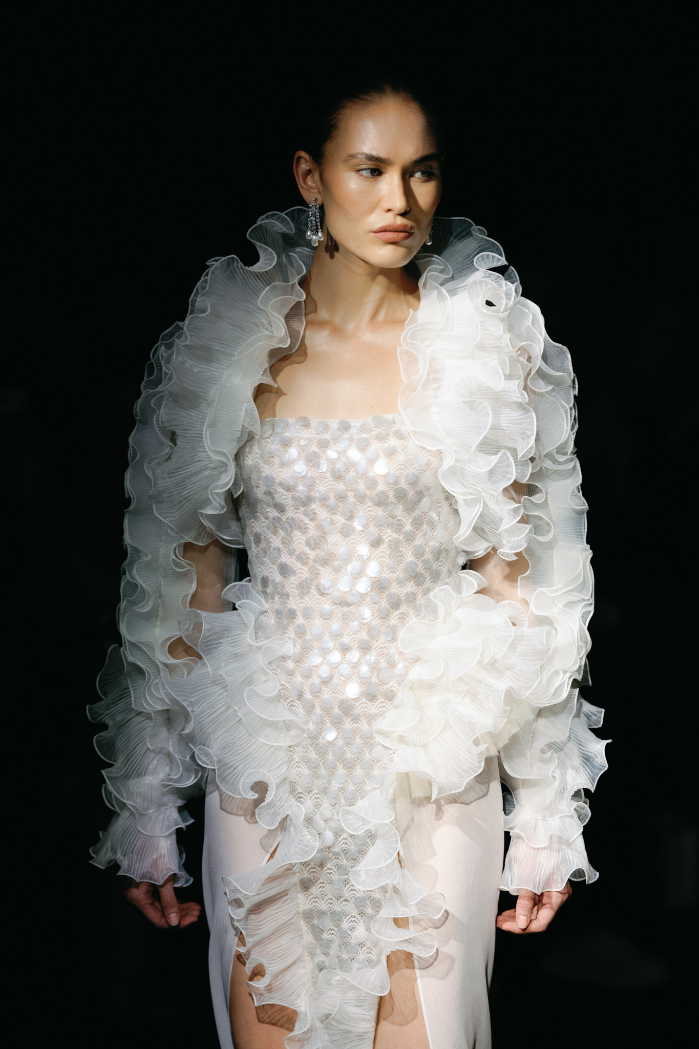 Model wearing an intricately embellished white bridal ensemble with dramatic floral-textured shoulders