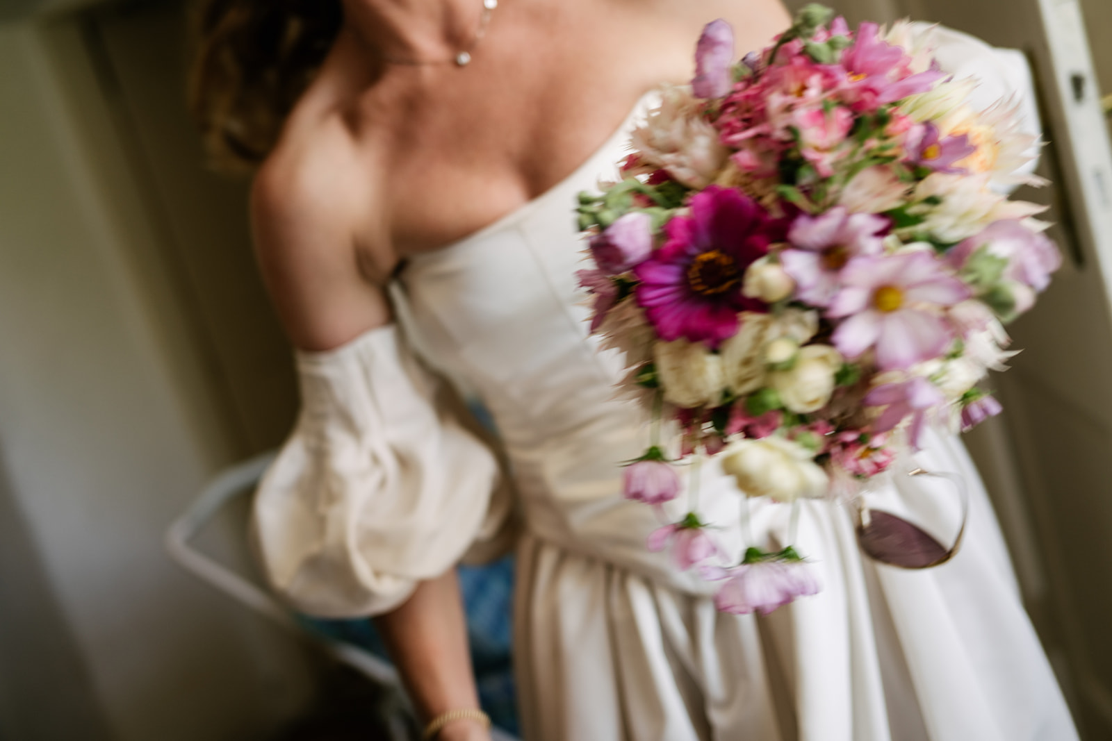 Close-up of a colorful pink and purple bridal bouquet paired with a romantic ivory wedding gown.
