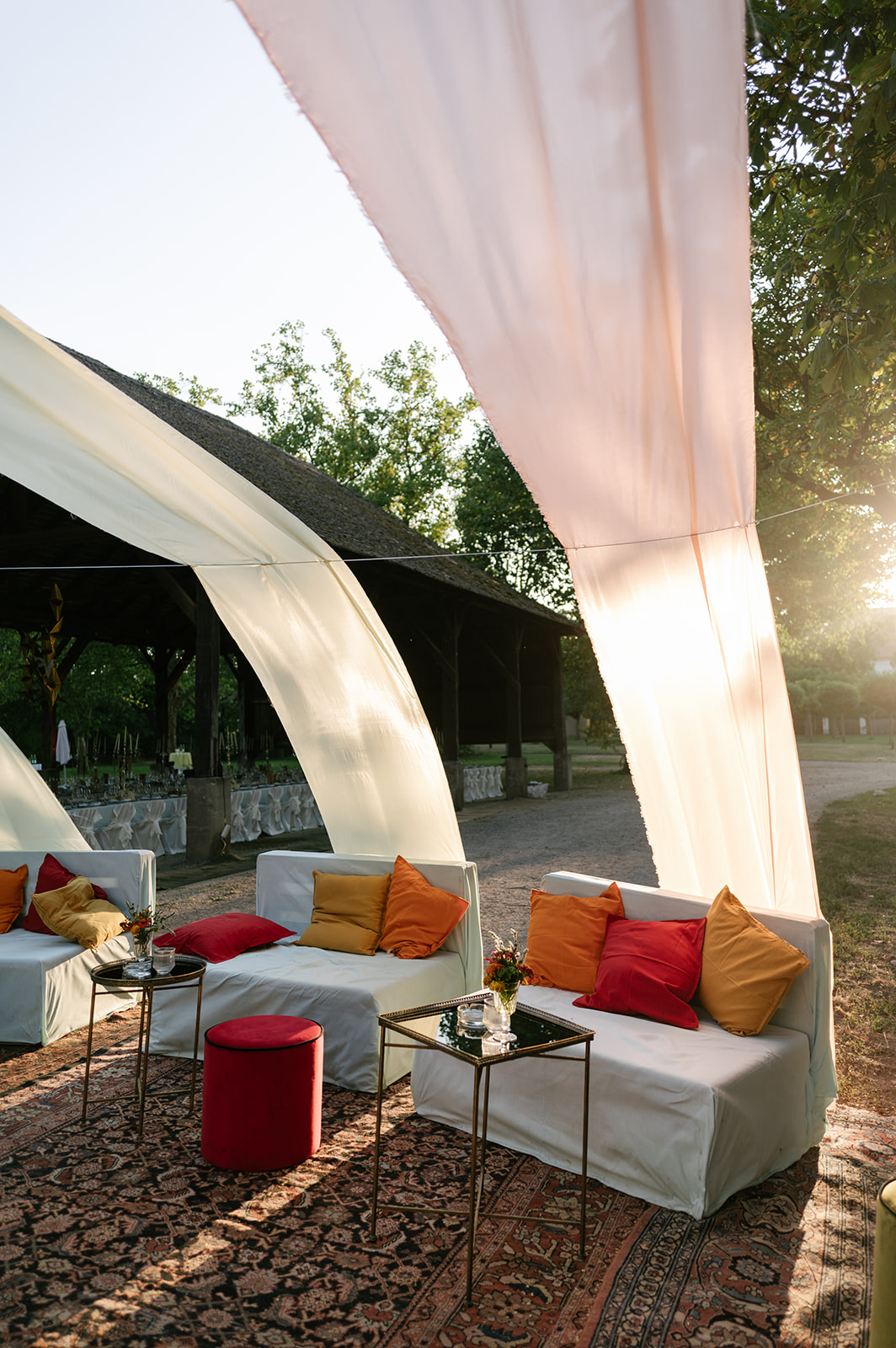 Italian-inspired outdoor wedding lounge with flowing ivory drapery, patterned rugs, and colorful cushions.
