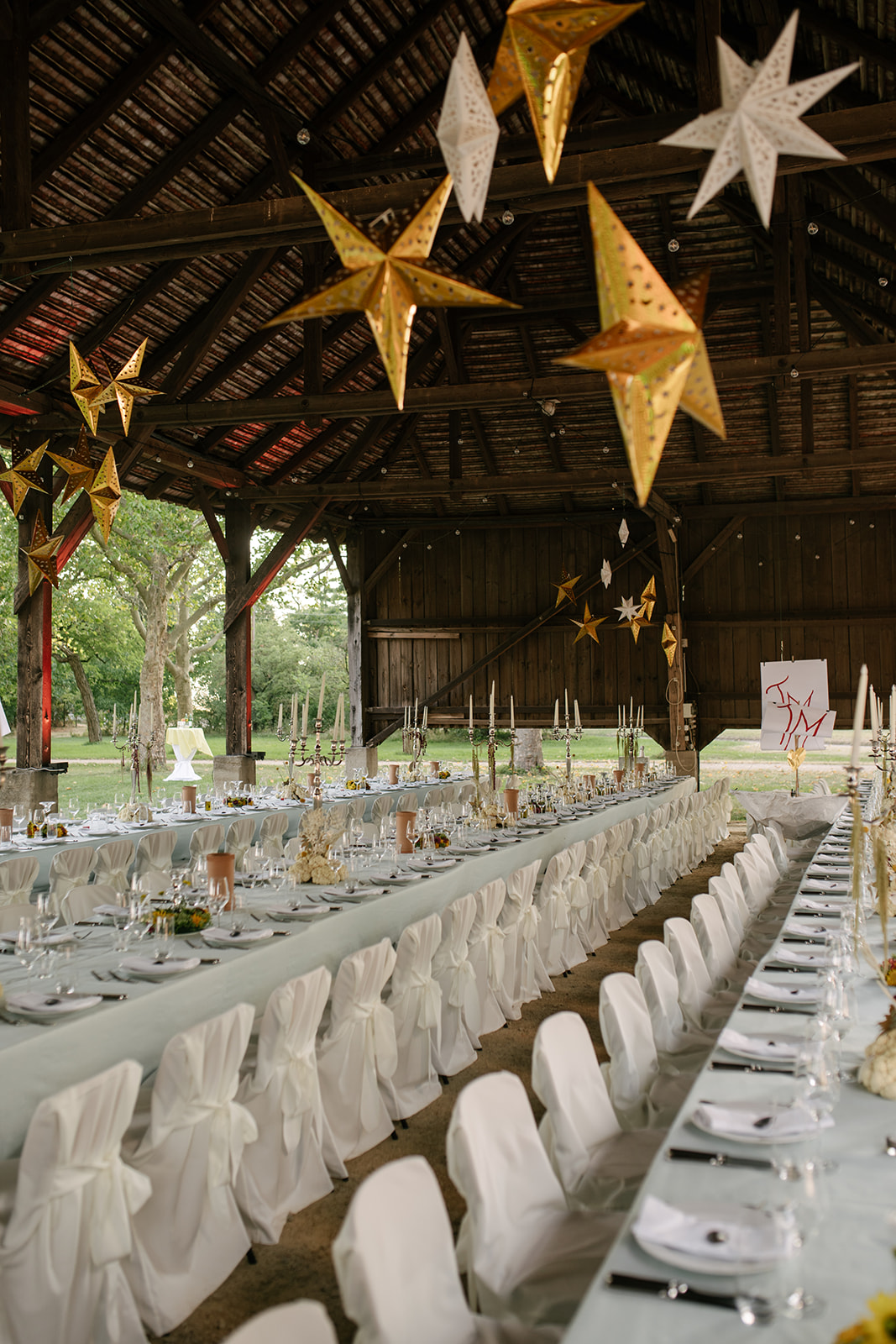 Long wedding reception tables beneath oversized golden stars inside a rustic Austrian barn.