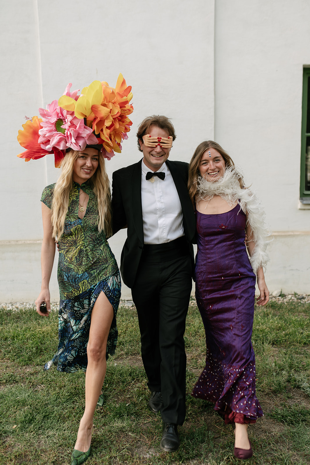 Wedding guest wearing a sculptural oversized floral headpiece alongside elegantly dressed guests at a surrealist-inspired celebration.