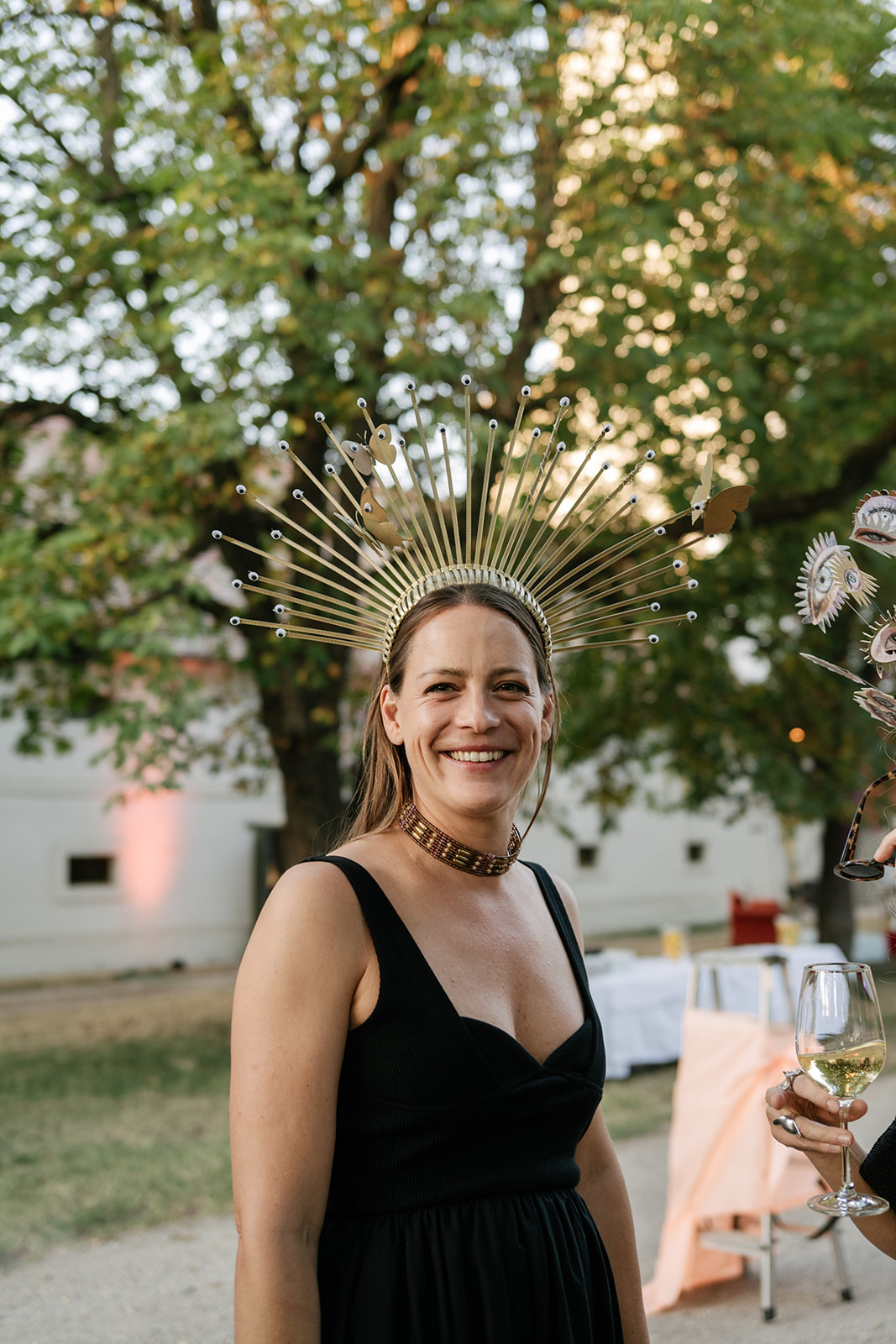 Smiling wedding guest wearing a dramatic gold sunburst crown and black dress at an artistic wedding celebration.