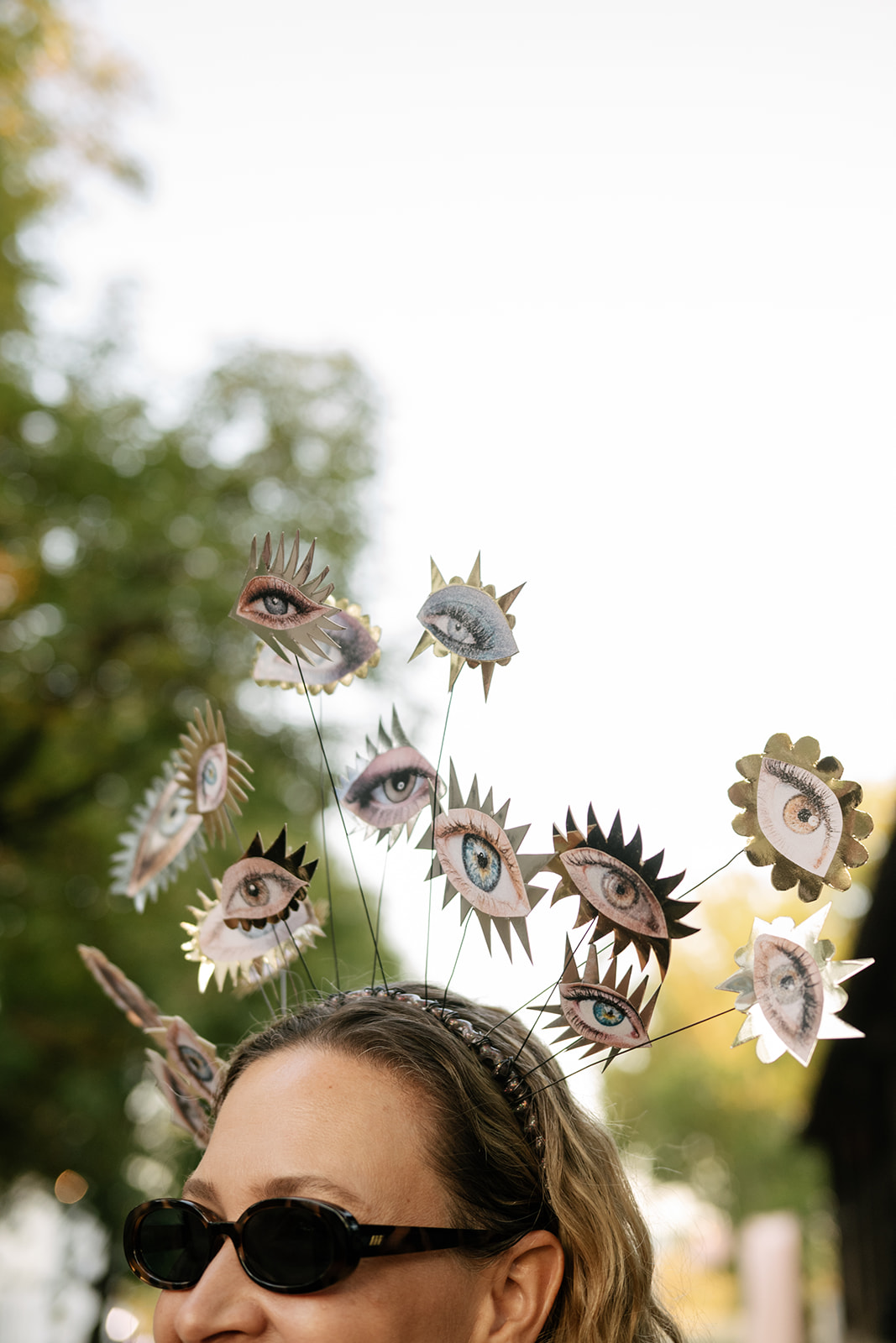 Close-up of an imaginative floral and eye-inspired sculptural headpiece worn by a wedding guest.