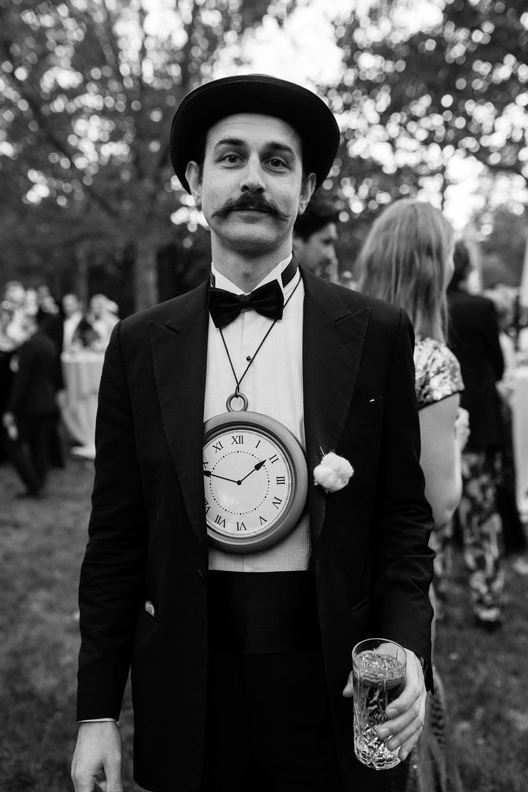 wedding guest in a top hat and tuxedo with an oversized pocket watch hanging from his jacket.